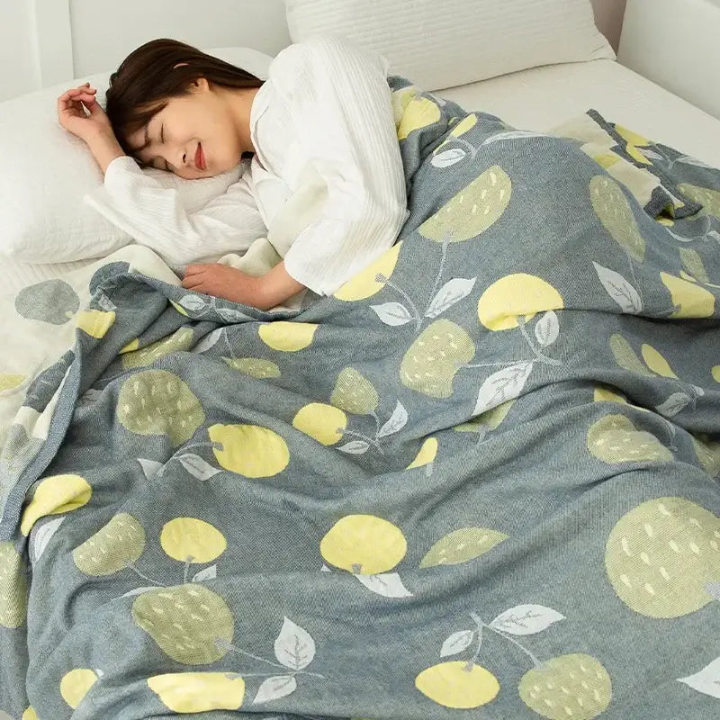 A cozy gray cotton gauze boho throw with yellow and green lemon pattern draped over a person in white nightgown