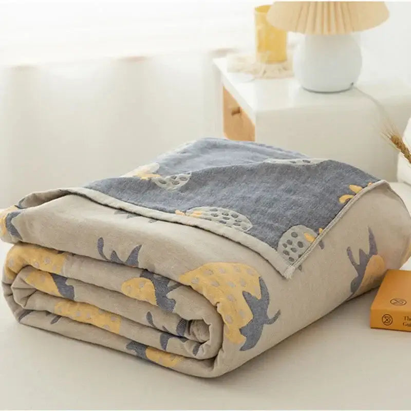 A soft folded cotton gauze boho throw blanket in beige and gray with yellow and blue pineapple bird decorbites cotton gauze