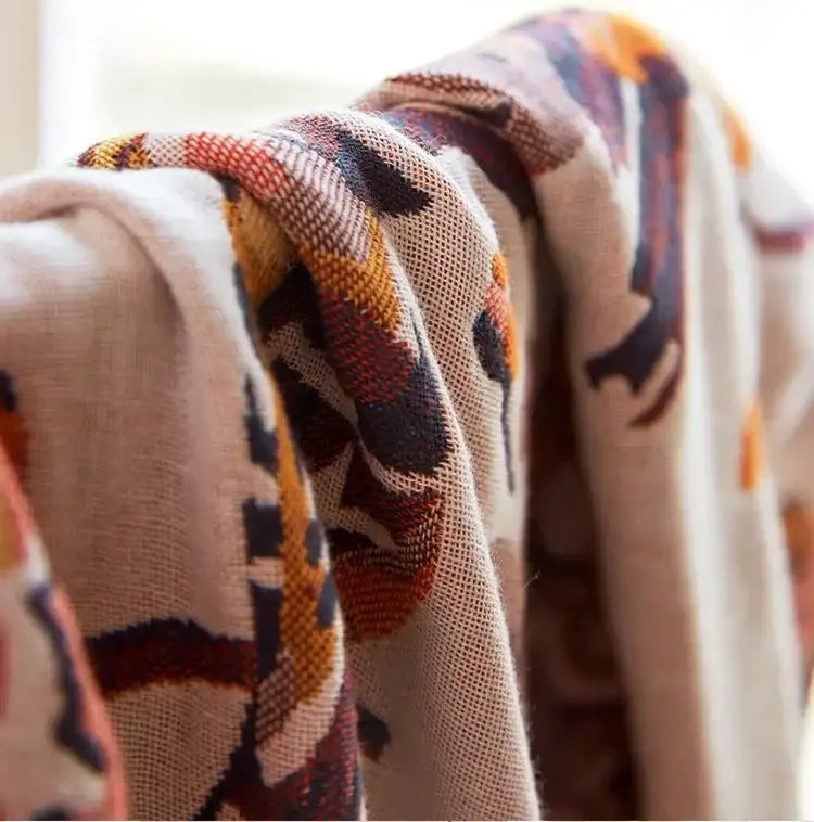 A cozy cream-colored cotton gauze peacock bath towel throw blanket featuring warm autumnal orange and rust patterns