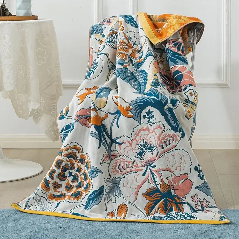 A decorbites cotton gauze bath towel with a vibrant peacock cream and orange floral pattern and yellow border