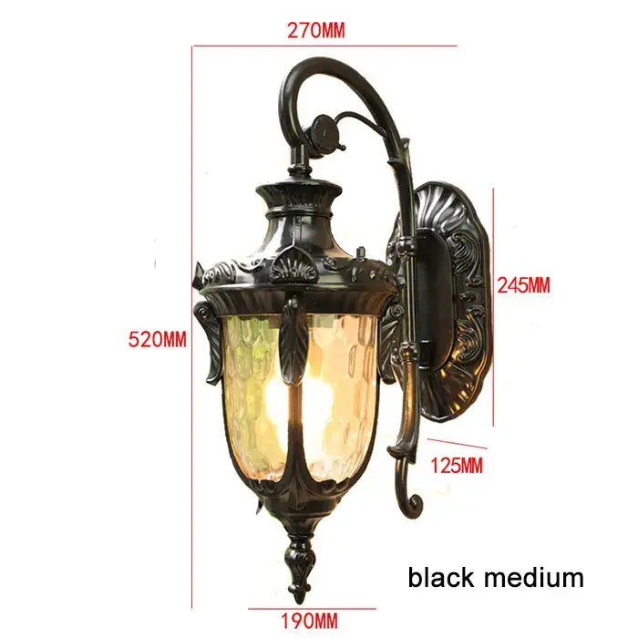 Country black wrought iron outdoor wall lantern with textured amber glass shade and ornate scrollwork detailing