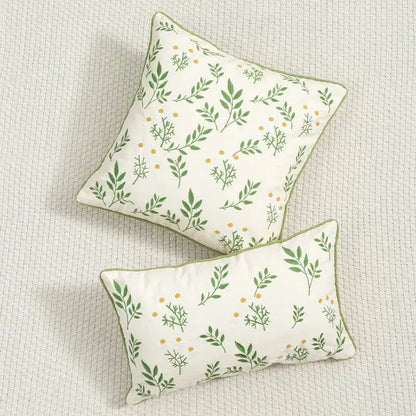 Cream-colored cushion cover with green leaf and yellow dot floral embroidered design and olive-green trim for living room