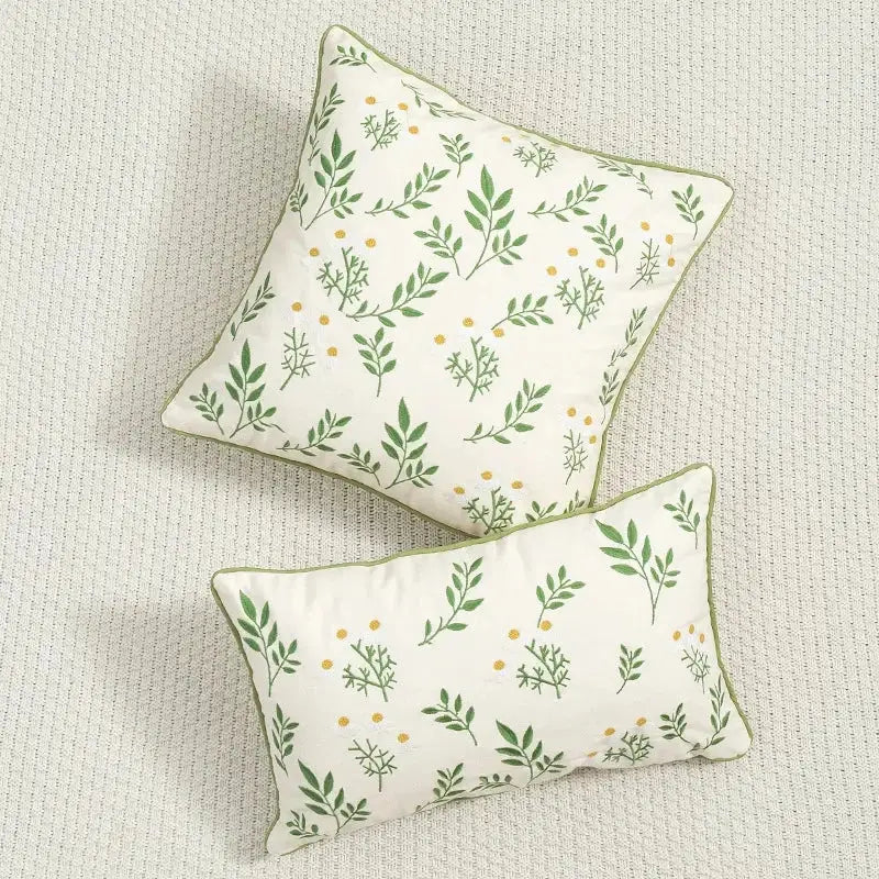 Cream-colored cushion cover with green leaf and yellow dot floral embroidered design and olive-green trim for living room