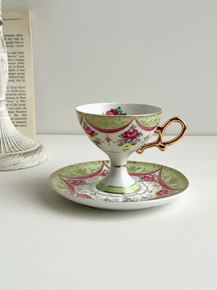 A delicate court style latte porcelain cup set with gold handle and pink green floral design on matching saucer