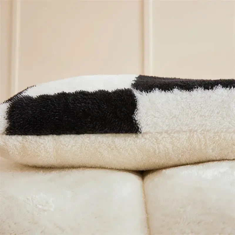 A cream-colored plush winter blanket with bold black and white stripes from decorbites cozy checkerboard winter collection
