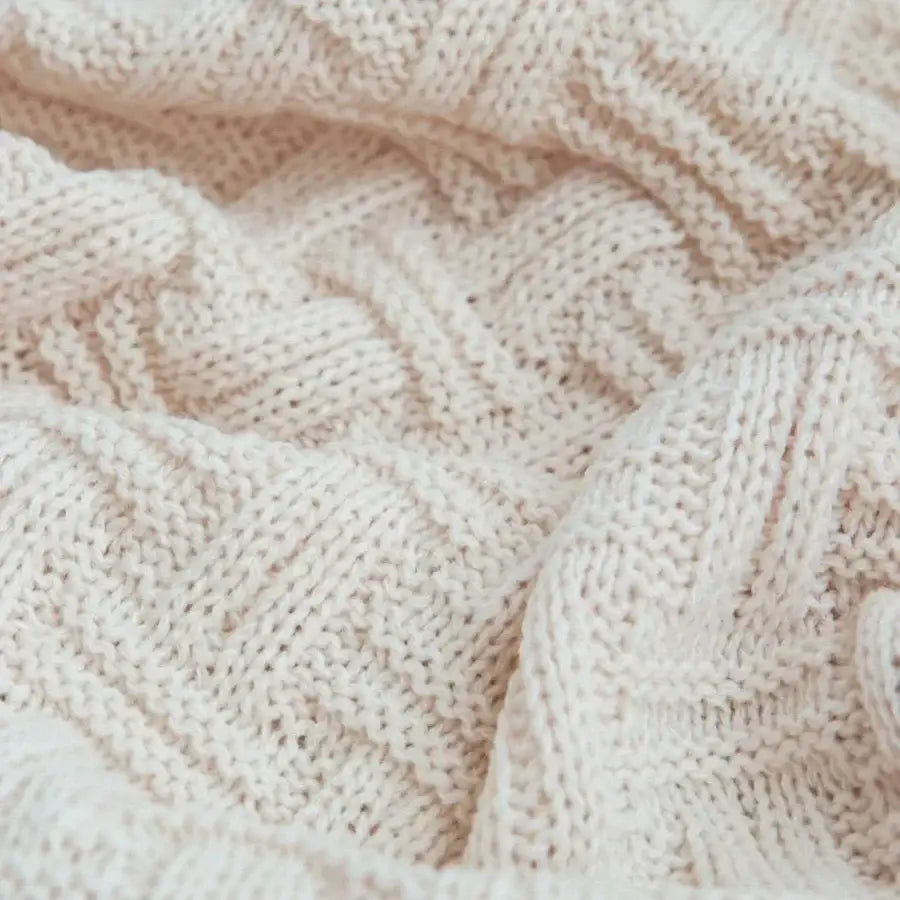 Cream-colored cable-knit sweater with soft textured weave paired with decorbites cozy fringed plaid throw blanket