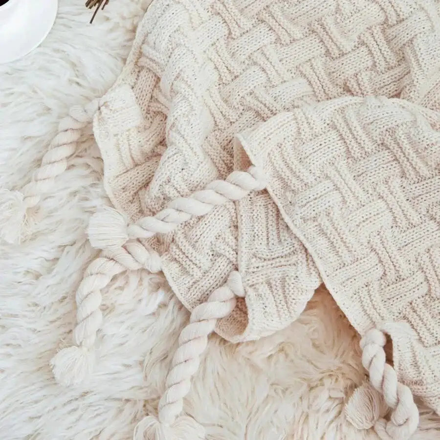 Cream-colored knitted beanie with woven texture and braided tassels complements decorbites cozy fringed plaid throw