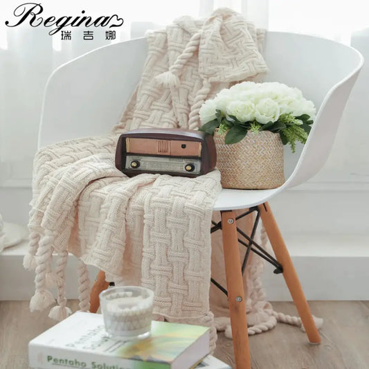 Cream-colored chunky knit cozy fringed plaid throw blanket with tassels draped over a white chair for bedroom decor