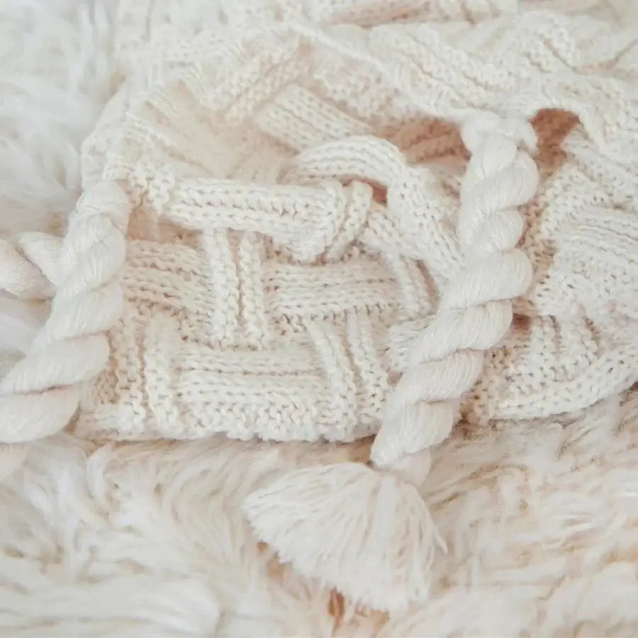 Cream-colored knitted cable-knit scarf with braided edges and tassel accent complements decorbites cozy fringed plaid throw