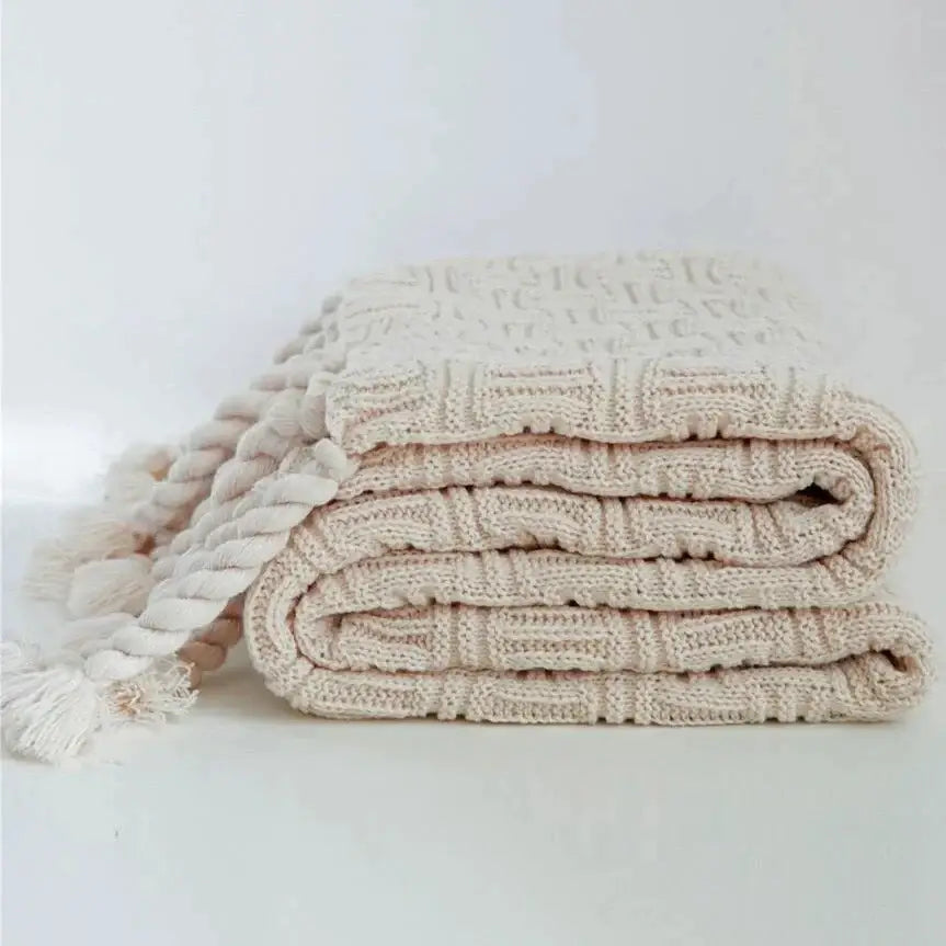 A cream-colored soft knit cozy fringed plaid throw blanket with textured pattern and thick braided rope tassel decorbites cozy fringed