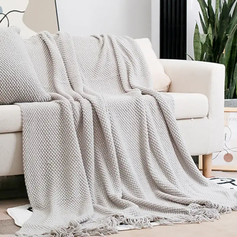 A soft light gray decorbites cozy knitted sofa blanket with textured waffle pattern and fringed tassel edges for living room decor