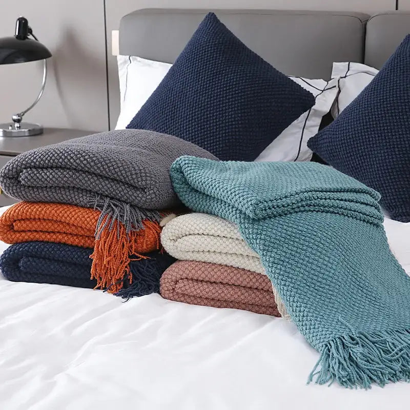 Stack of decorbites cozy knitted sofa blankets in muted gray teal orange and navy blue with textured tassels