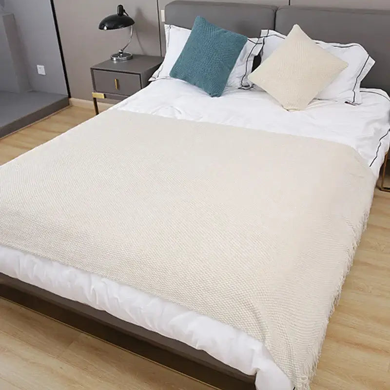 Cream-colored decorbites cozy knitted sofa blanket with textured knit and fringed edges for living room decor