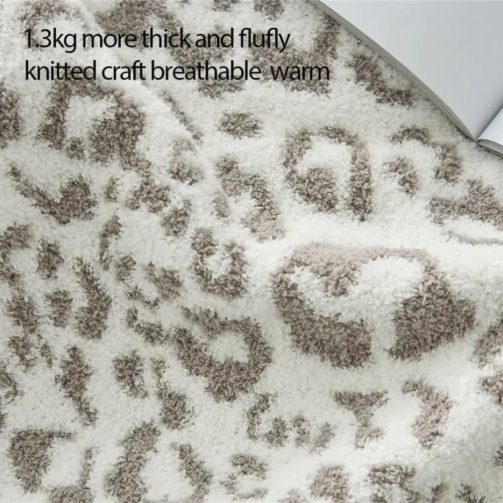 A plush cozy leopard print knitted cream and gray throw blanket with a soft white and beige leopard print pattern