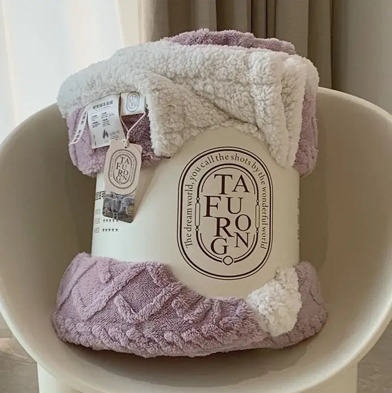 A soft lavender and white coral fleece blanket with a textured plush surface and cozy rolled-up design