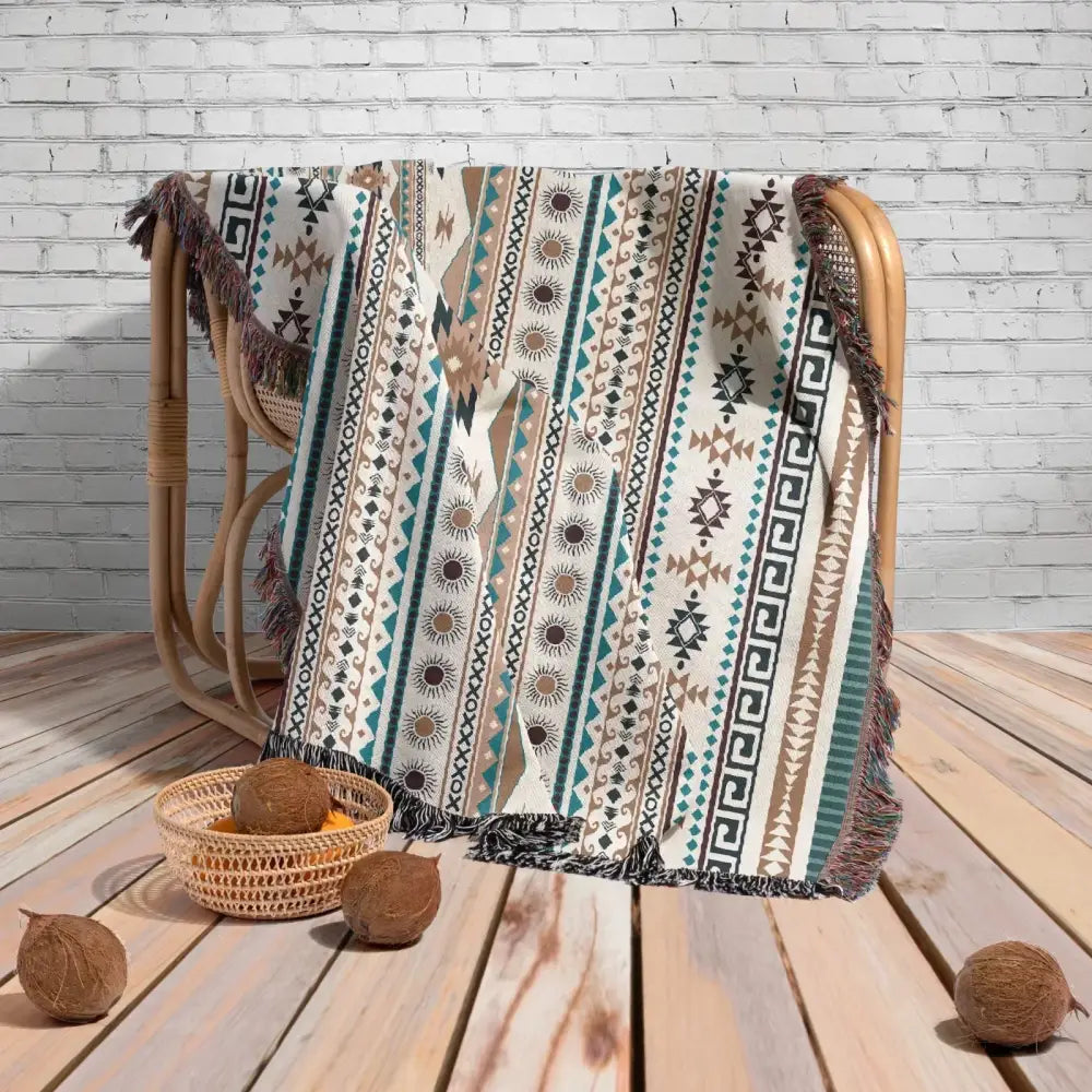 A cream woven throw blanket with teal brown and black geometric and sunburst patterns and fringed edges for cozy nordic camping decorbites cozy nordic