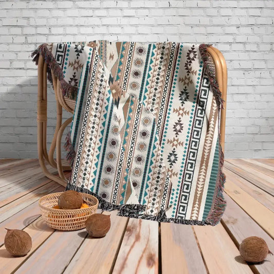 A cream woven throw blanket with teal brown and black geometric and sunburst patterns and fringed edges for cozy nordic camping decorbites cozy nordic