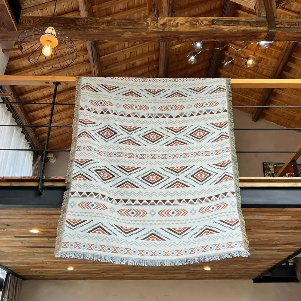 A cream woven throw blanket with a terracotta geometric pattern and fringed edges for cozy nordic camping decorbites