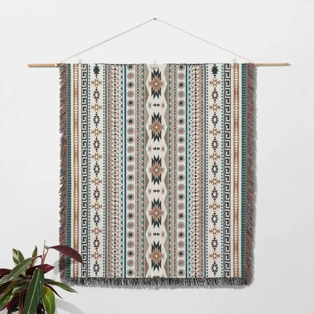 A woven cozy nordic camping blanket in earthy beige, teal, brown with tribal patterns and fringed edges hanging decorbites cozy nordic