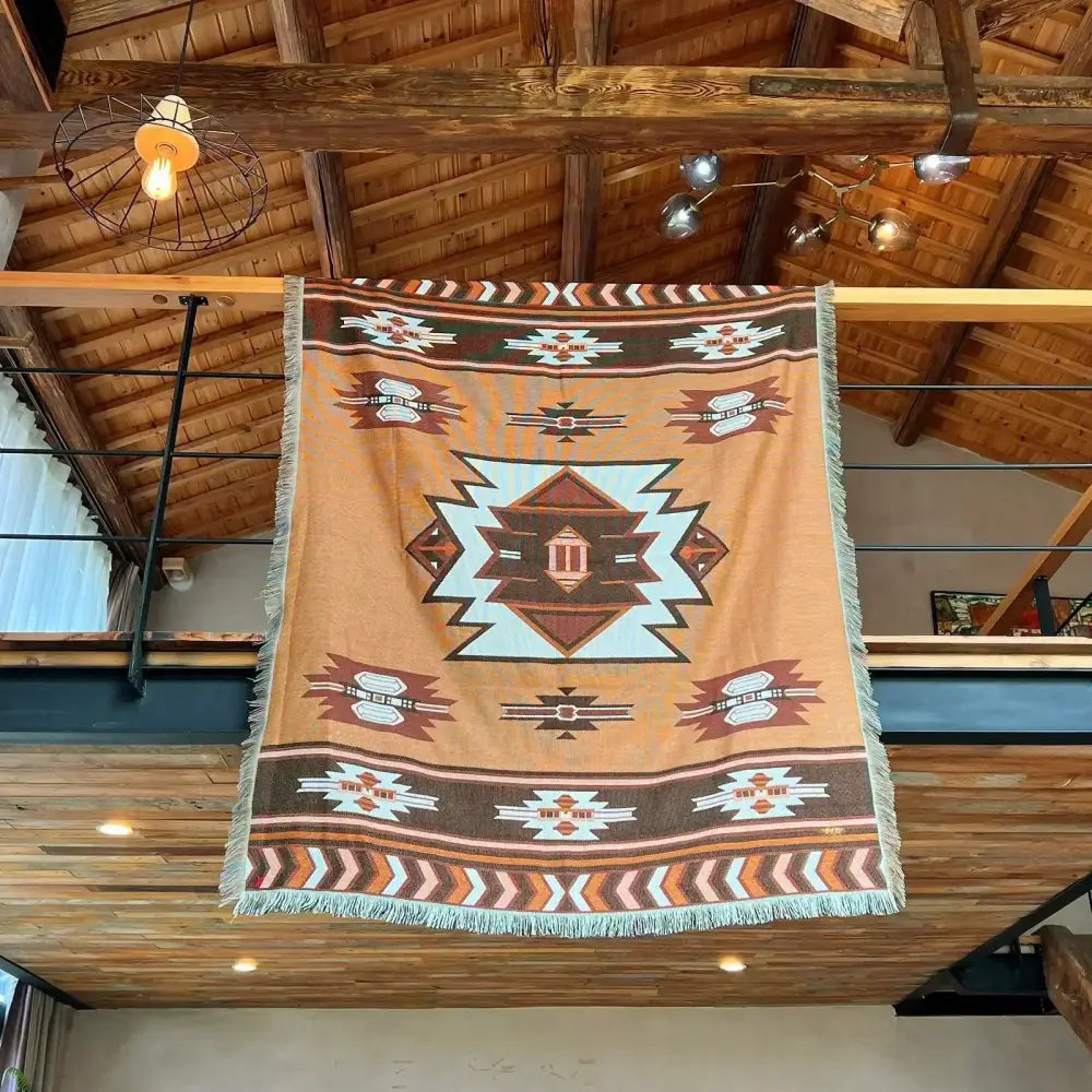 A tan and brown geometric nordic camping blanket with fringed edges and a central light blue diamond motif for cozy nordic decorbites living room decor