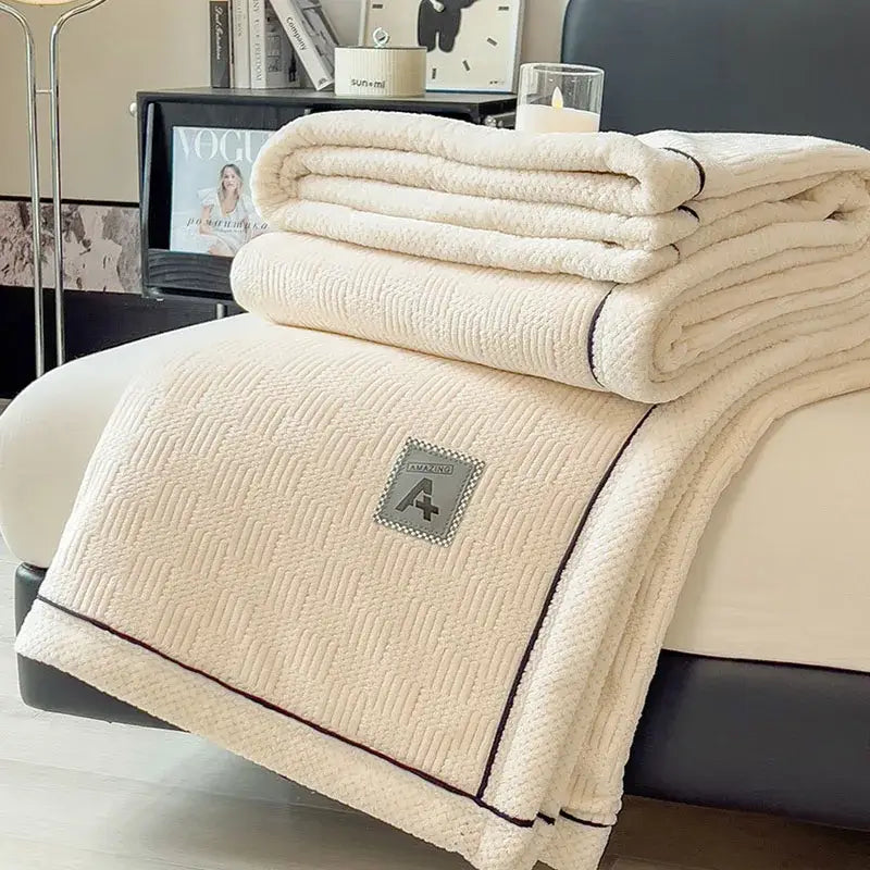 Cream-colored plush quilted blanket with dark trim and embroidered patch featuring decorbites cozy striped velvet