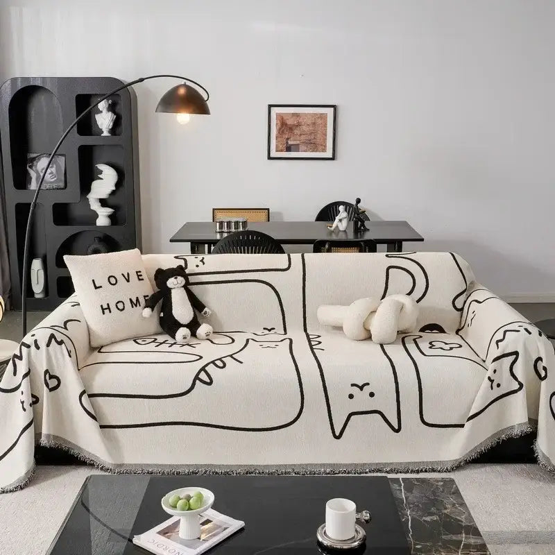 Cream-colored chenille sofa cover with black line-drawn cat illustrations and fringed edges for living room use