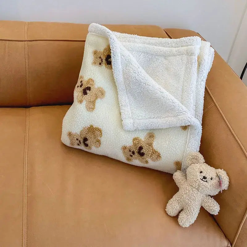Cream and brown bear lamb plush blanket with soft sherpa texture folded on tan leather couch with matching stuffed toy