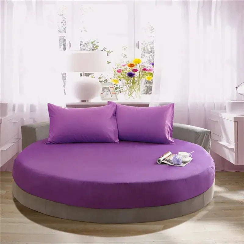 Purple round fitted bed with matching pillows and gray base featuring cream and gray round fitted bed sheet set