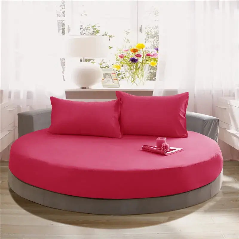 Vibrant fuchsia round bed with matching pillows and gray upholstered frame featuring a cream and gray fitted bed sheet set