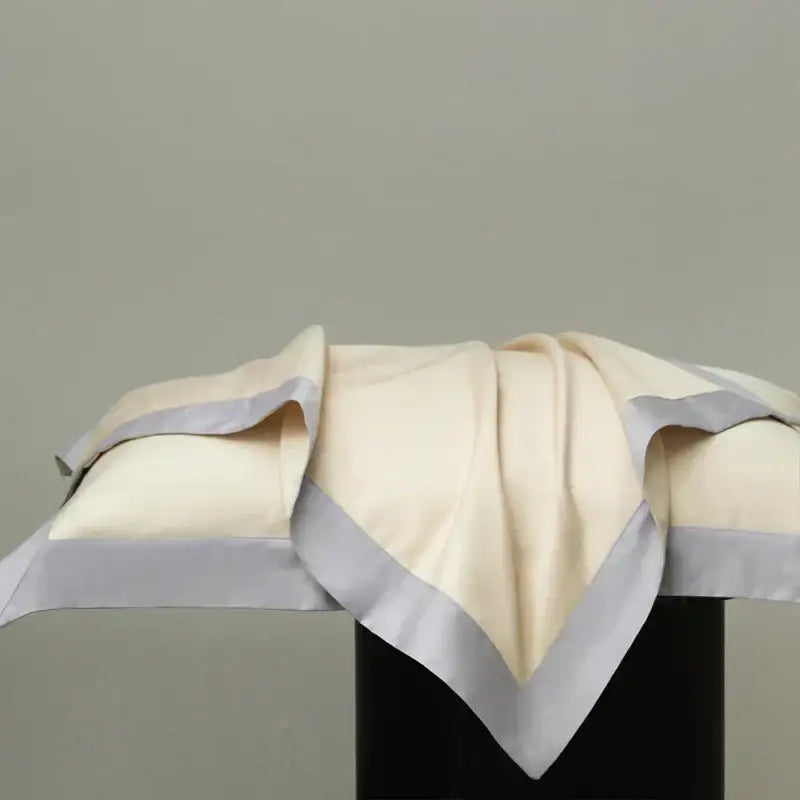 Cream-colored silk pillowcase with light gray trim in a cream and lavender egyptian cotton hotel style bedding set