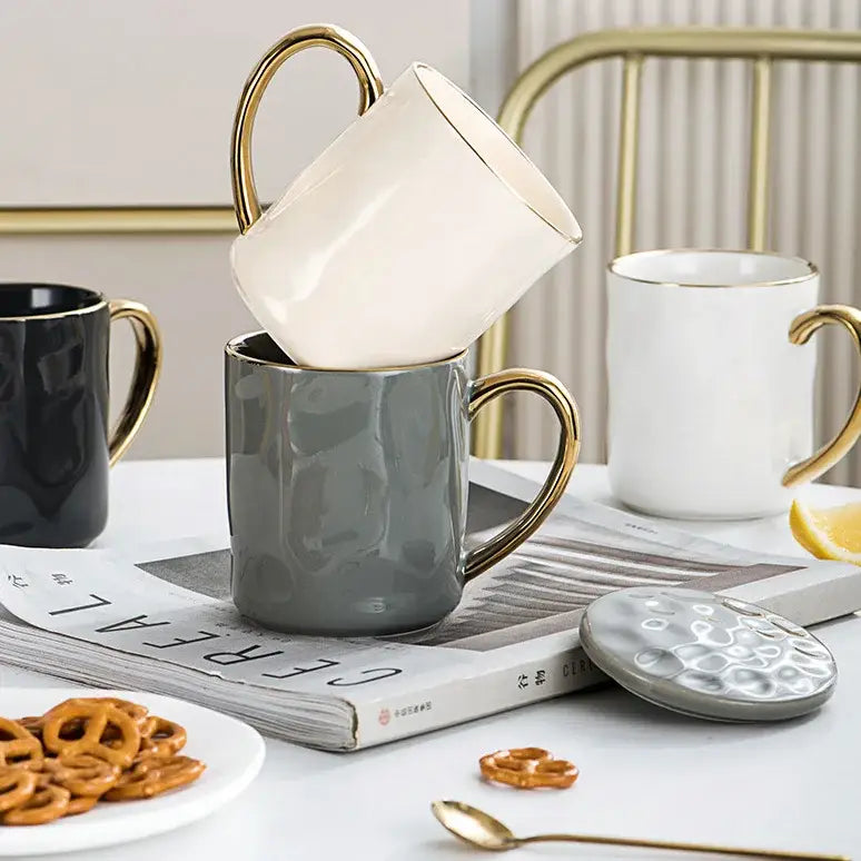 A cream and navy ceramic rim mug set featuring a white nordic gold rim mug stacked on a gray textured coffee cup
