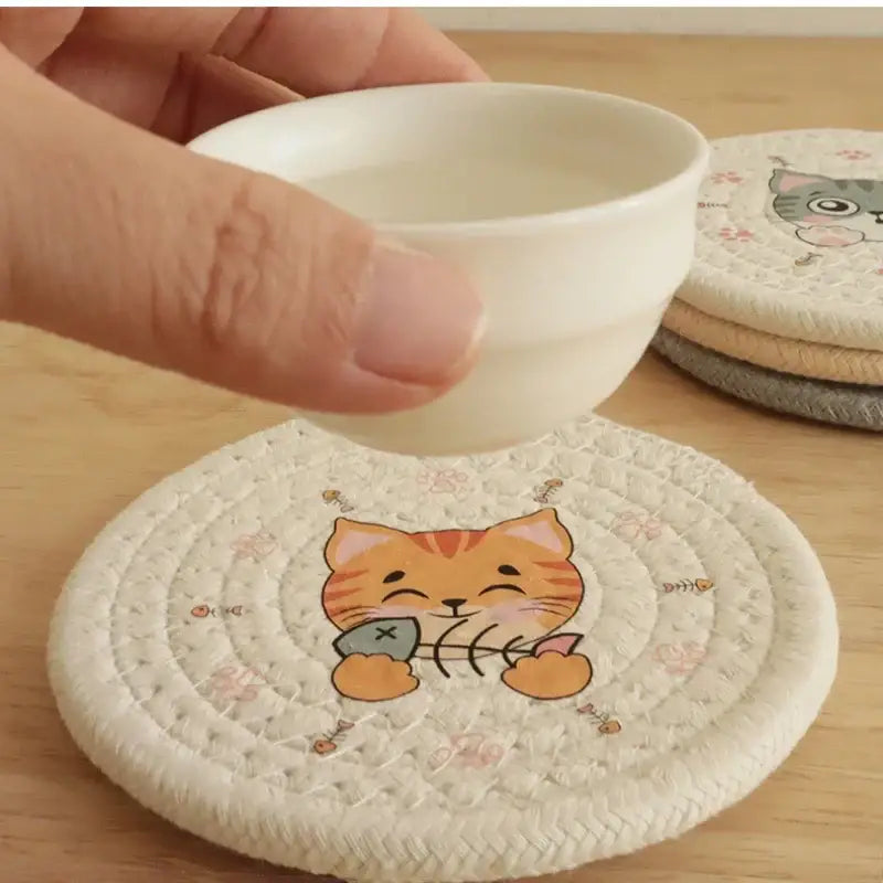 Cream braided rope cat print round coaster with cream woven base featuring cartoon orange tabby and fish decorbites cat print