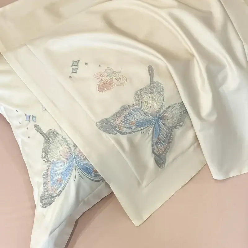 Cream-colored satin pillowcases with decorbites butterfly embroidery in blue silver and peach in a bedding set