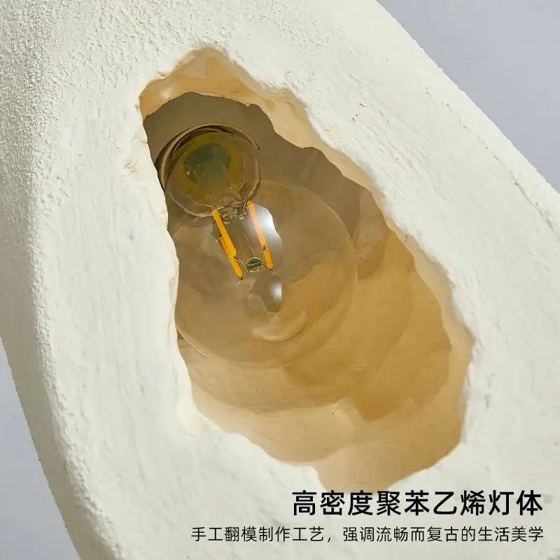 A warm amber glowing led filament bulb inside a textured cream ceramic pendant light decorbites cement handmade housing