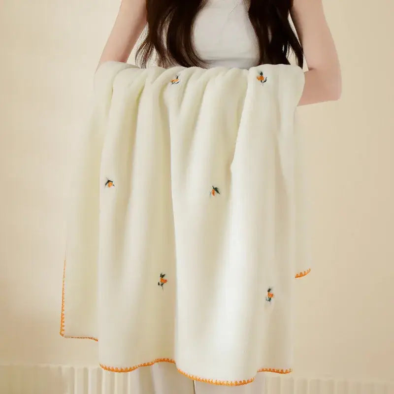Cream-colored velvet embroidered blanket with delicate orange and green citrus motifs and scalloped edges pom pom throw