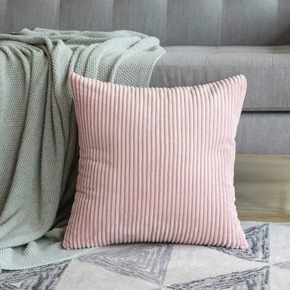 A soft pink decorbites corduroy striped cushion cover with vertical ridges resting beside a gray sofa on a rug
