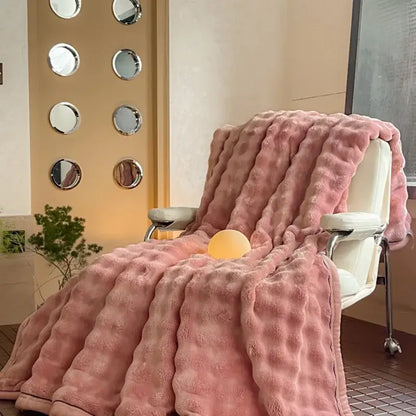 A plush soft pink cream cozy bubble faux rabbit fur blanket with a textured quilted pattern draped on a white chair