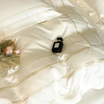 Black rectangular perfume bottle with silver cap resting on cream embroidered ice silk bedding set with gold leaf design