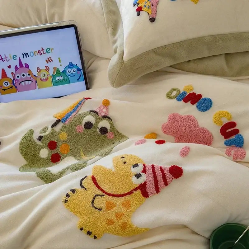 Cream embroidered milk fleece bedding set with white plush blanket featuring colorful cartoon monsters and dinosaur lettering