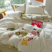 Cream embroidered milk fleece bedding set with plush duvet featuring cartoon dinosaurs and colorful pom-pom accents