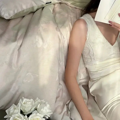 A delicate ivory satin dress with lace trim and v-neckline displayed alongside cream floral cotton jacquard bedding set