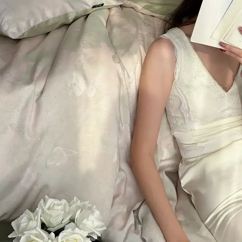 A delicate ivory satin dress with lace trim and v-neckline displayed alongside cream floral cotton jacquard bedding set