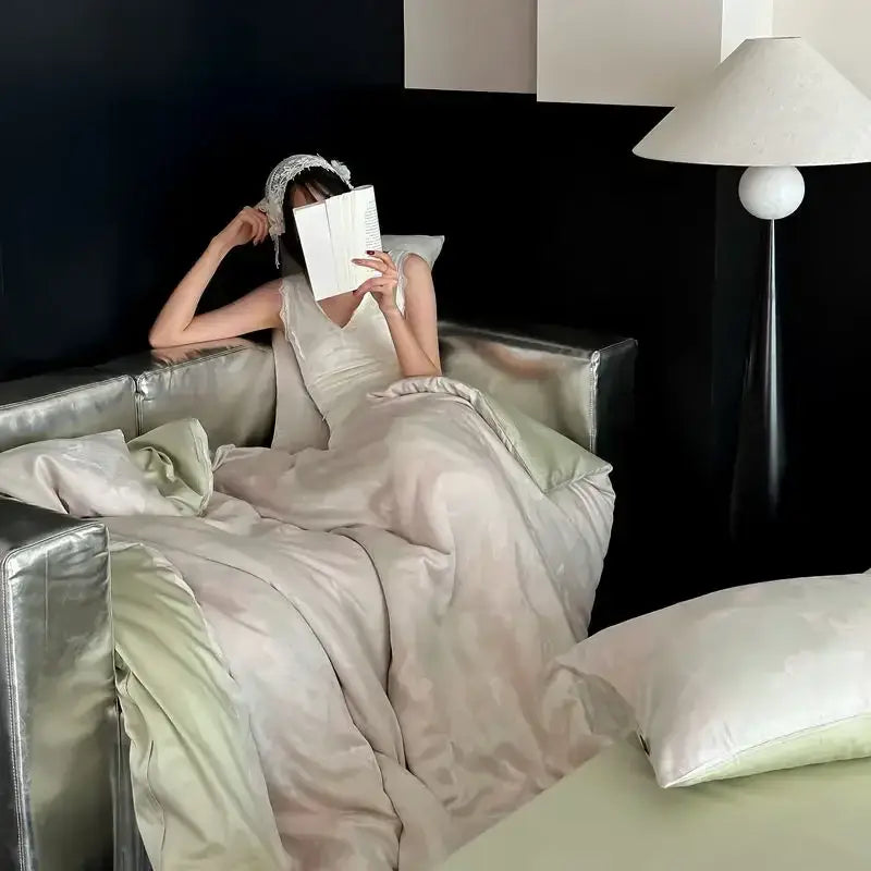 A woman in an off-white satin gown sits on a silver sofa beside a cream floral cotton jacquard bedding set