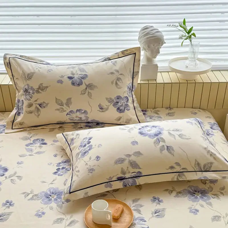 Cream flower print satin bed cover with cream pillowcases featuring delicate purple and gray florals and black border