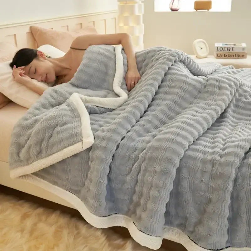 Soft gray plush rabbit plush quilted blanket with white fleece lining and ribbed texture draped over a sleeping woman