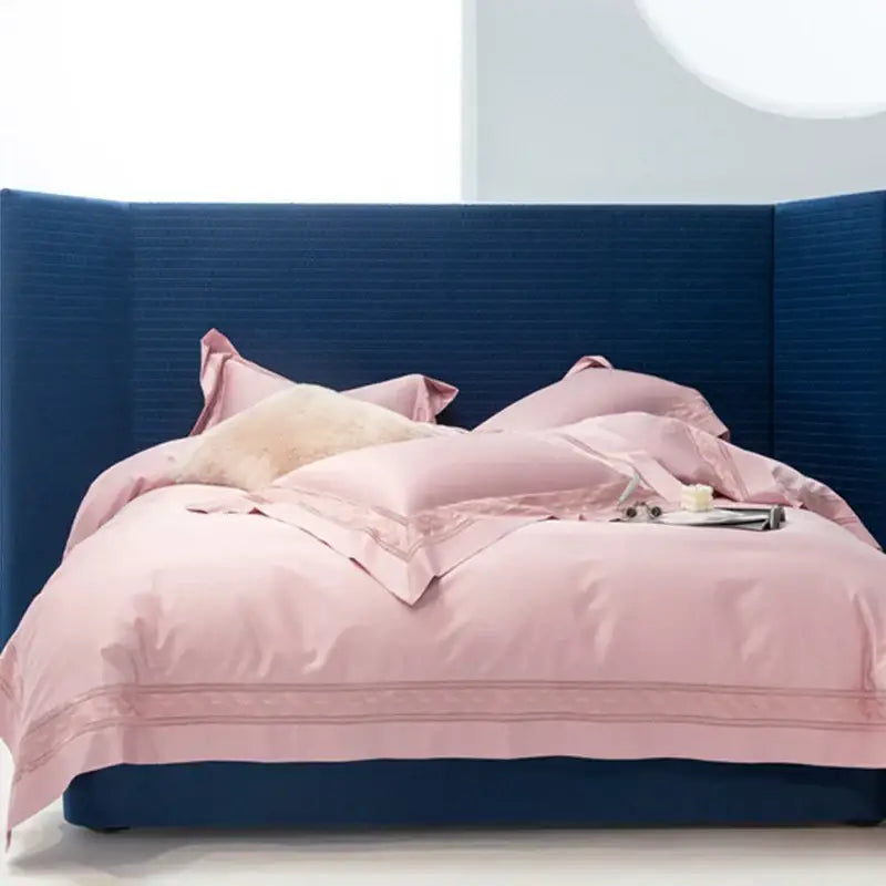 A plush pink satin decorbites bedding set with cream gold embroidery and fluffy pillow against a blue headboard in two sizes