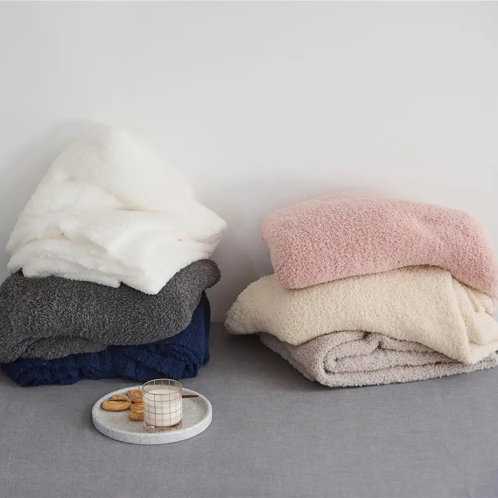 Stacks of plush knitted throw blankets in cream white gray navy beige and pink made of soft ribbed microfiber fleece