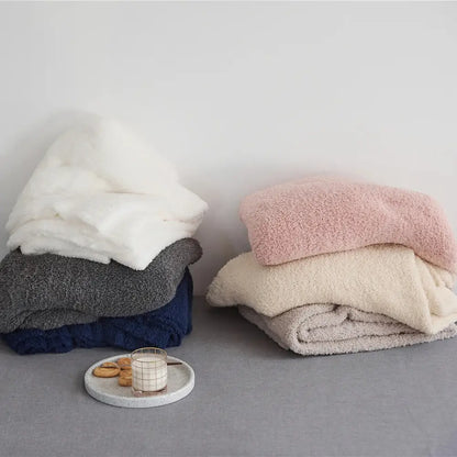 Stacks of plush knitted throw blankets in cream white gray navy beige and pink made of soft ribbed microfiber fleece