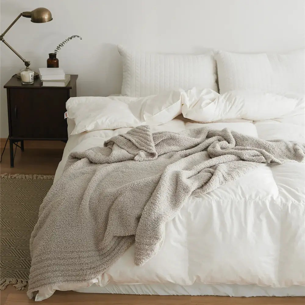 Soft gray knitted throw blanket made of plush microfiber ribbed quilt draped over a bed with white linens