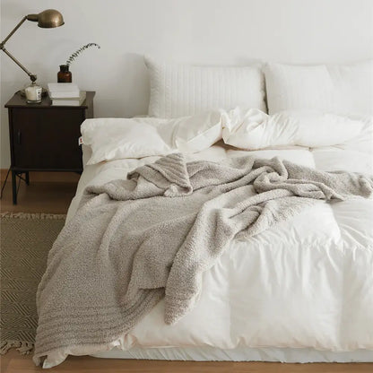 Soft gray knitted throw blanket made of plush microfiber ribbed quilt draped over a bed with white linens